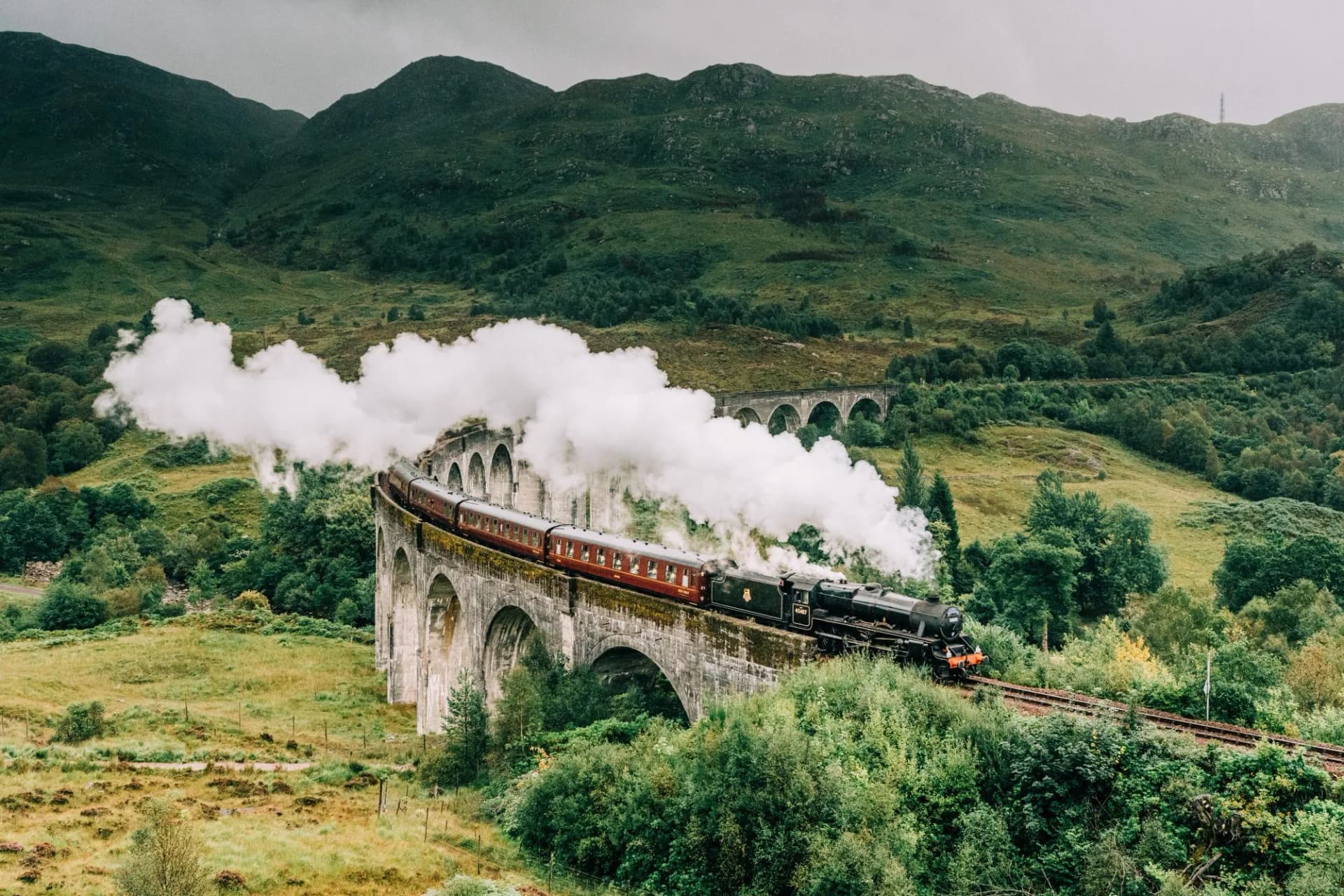 Jacobite steam train crossing Glenfinnan Viaduct in Scottish Highlands with steam billowing