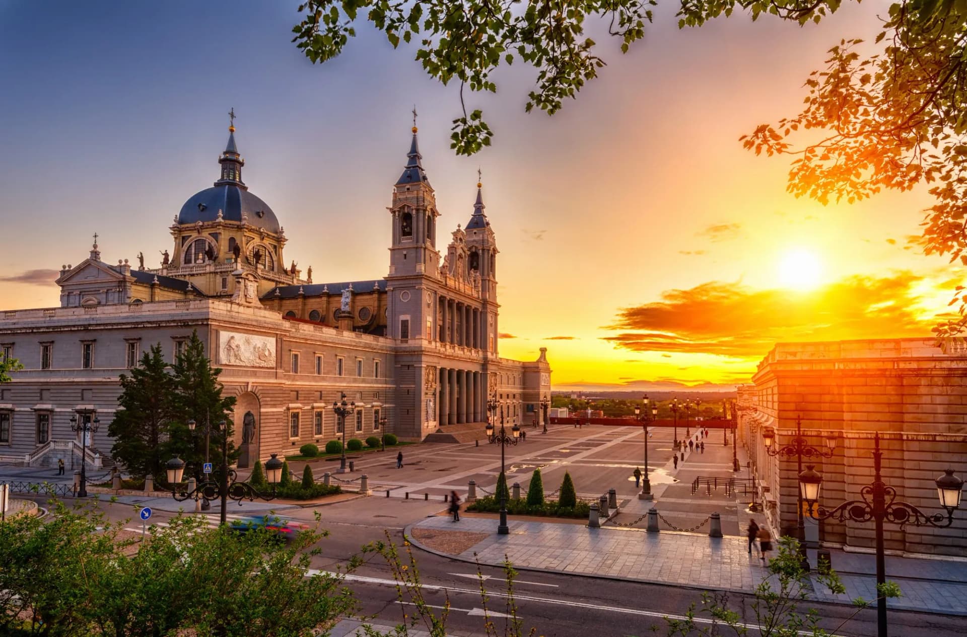 Sunset view of Almudena Cathedral in Madrid, Spain, with sun setting over the plaza.