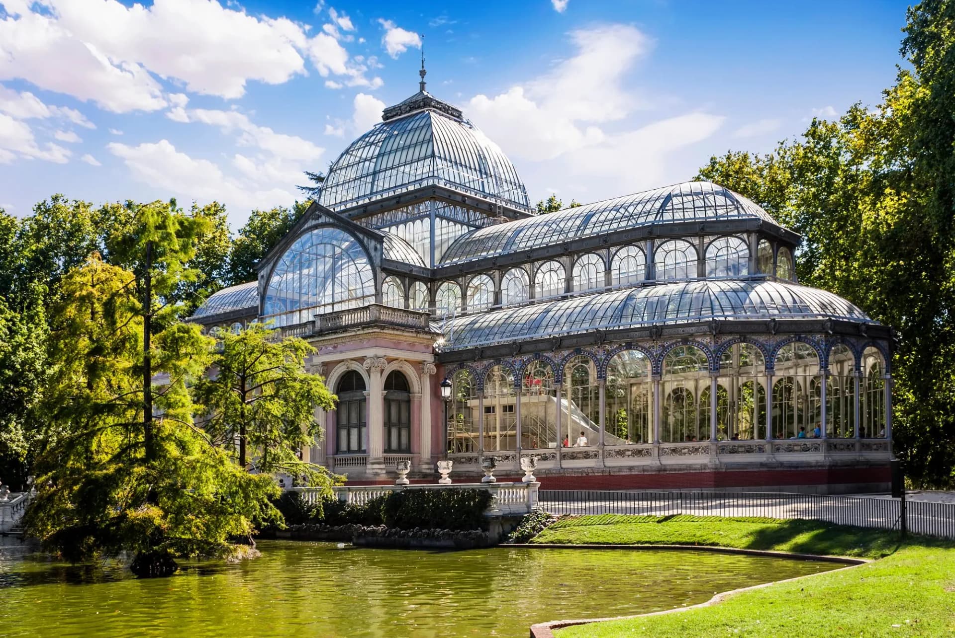 Crystal Palace in El Retiro Park, Madrid, reflected in a pond under a blue sky.