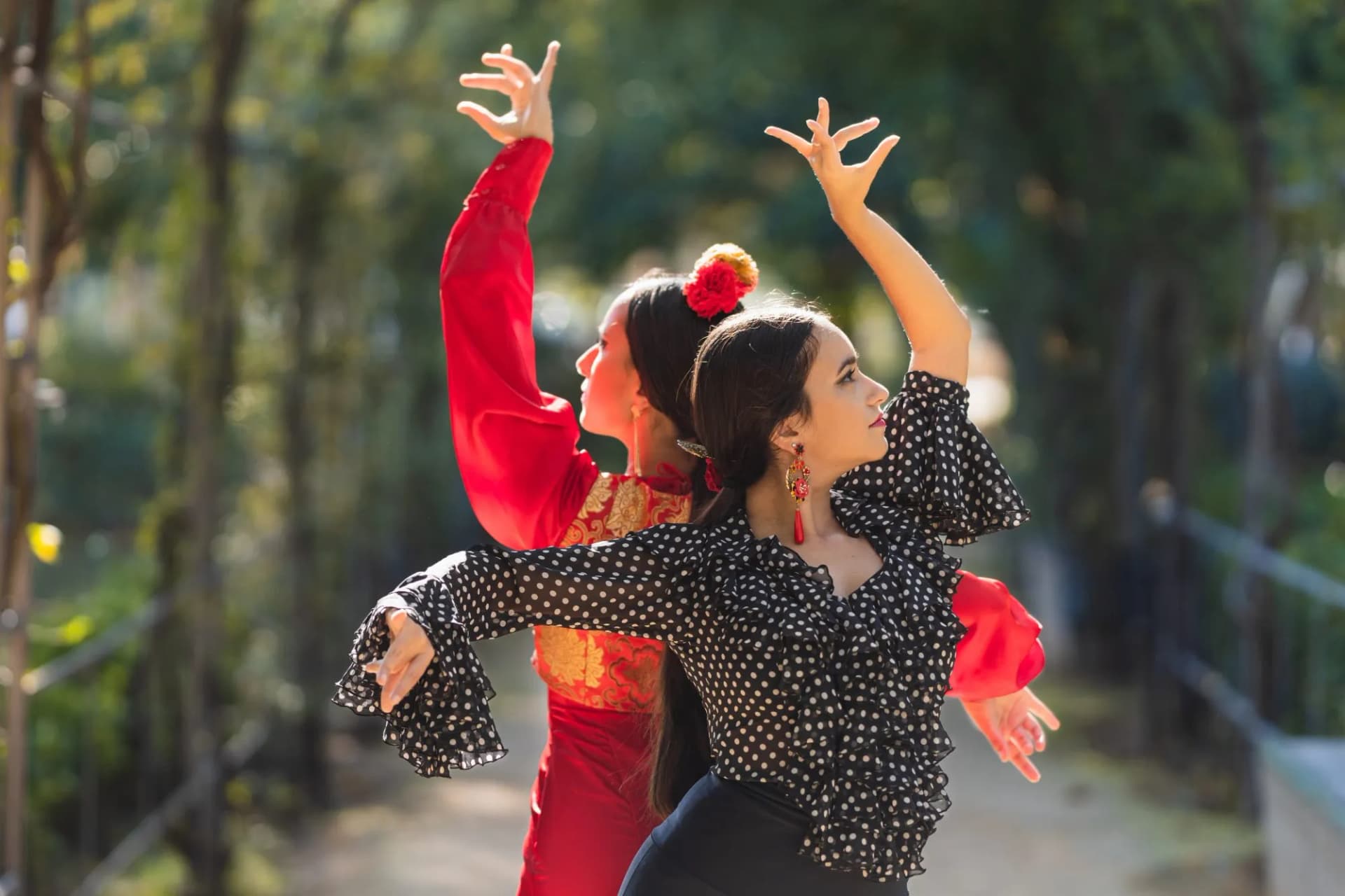 Two female flamenco dancers performing choreography outdoors with trees in the background.
