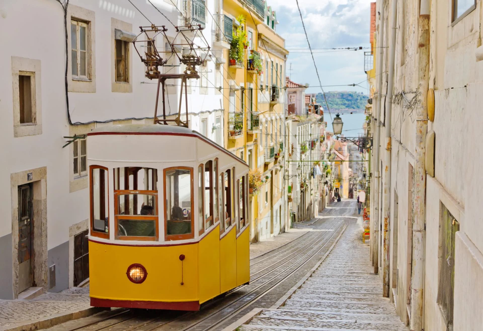 Yellow funicular ascending steep cobblestone street between historic buildings in Lisbon.
