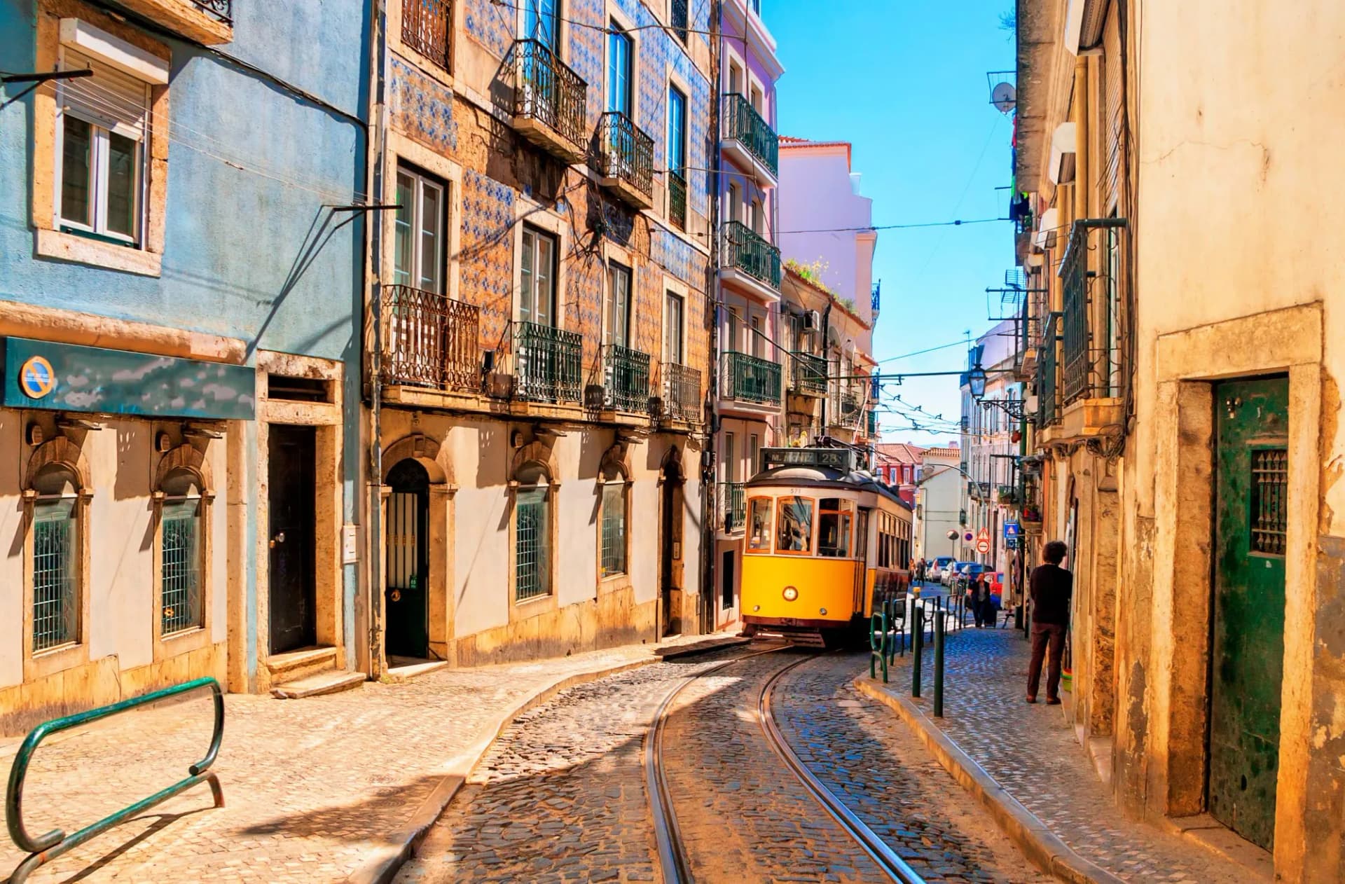 Vintage yellow tram on cobblestone street in Lisbon, Portugal, lined with tiled buildings.