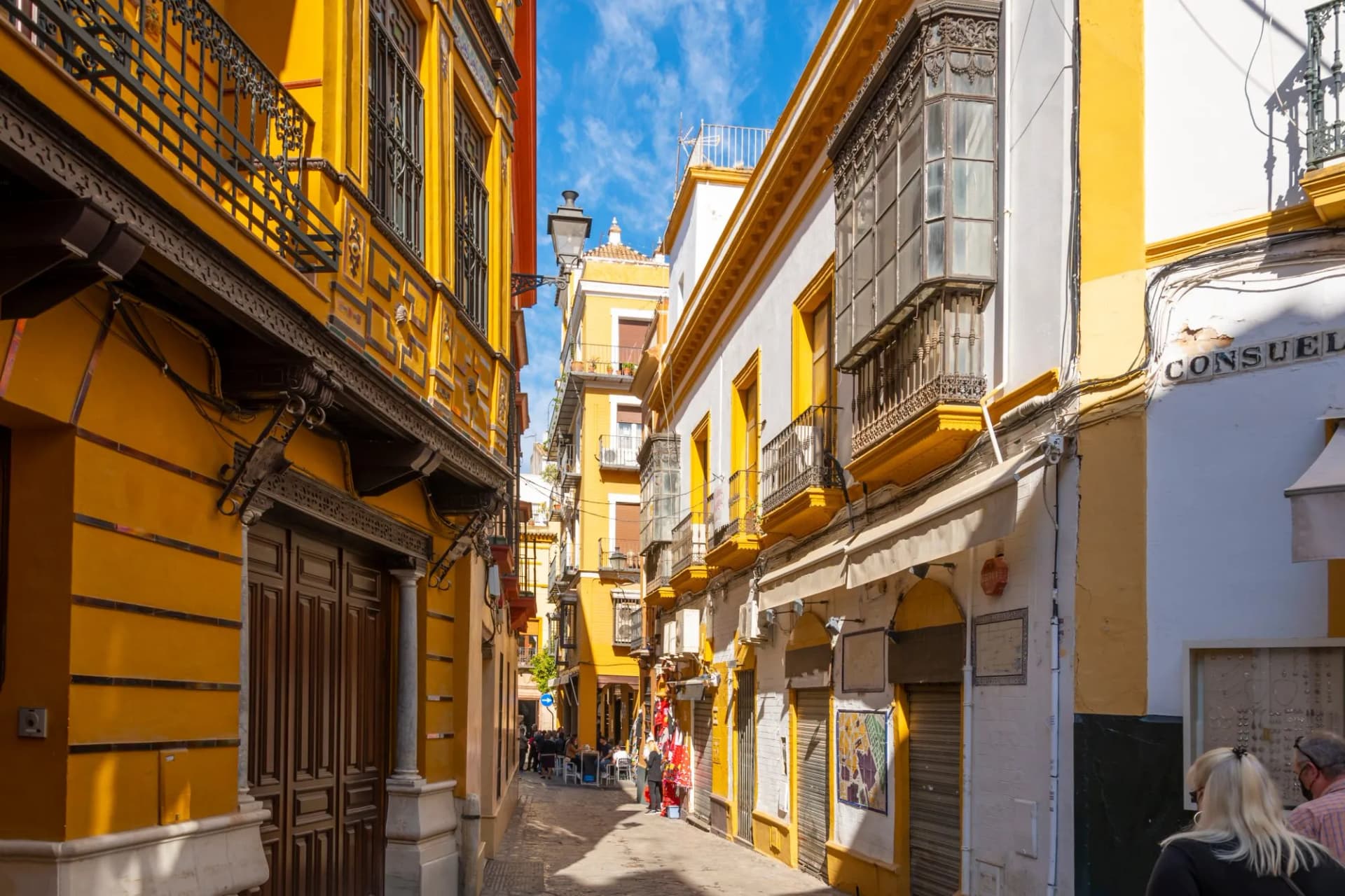 Colorful yellow and white buildings line a narrow street in Seville's Barrio Santa Cruz district.
