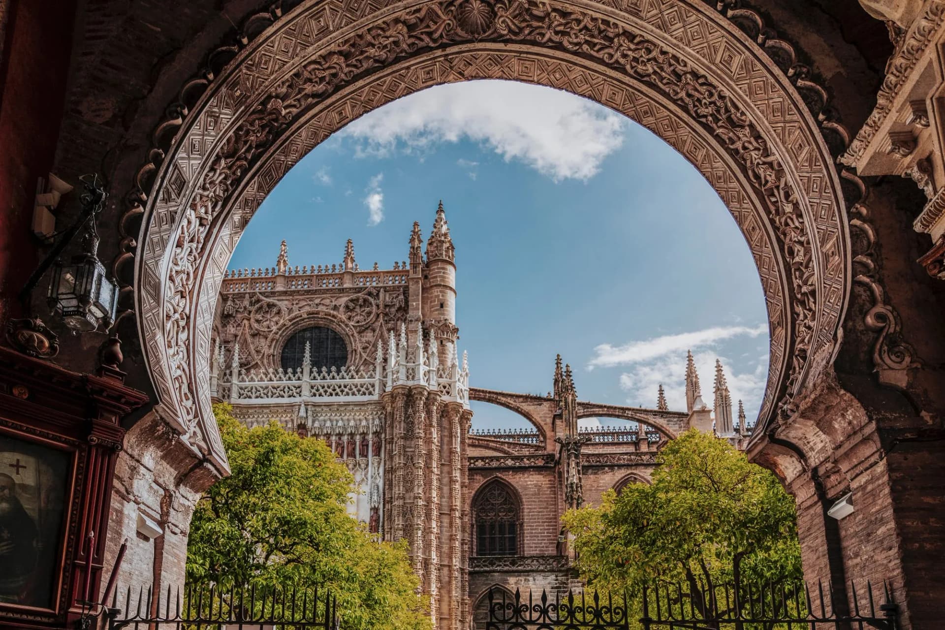 View of Seville Cathedral North Facade through an ornate arch gate in the orange courtyard, Andalusia, Spain.
