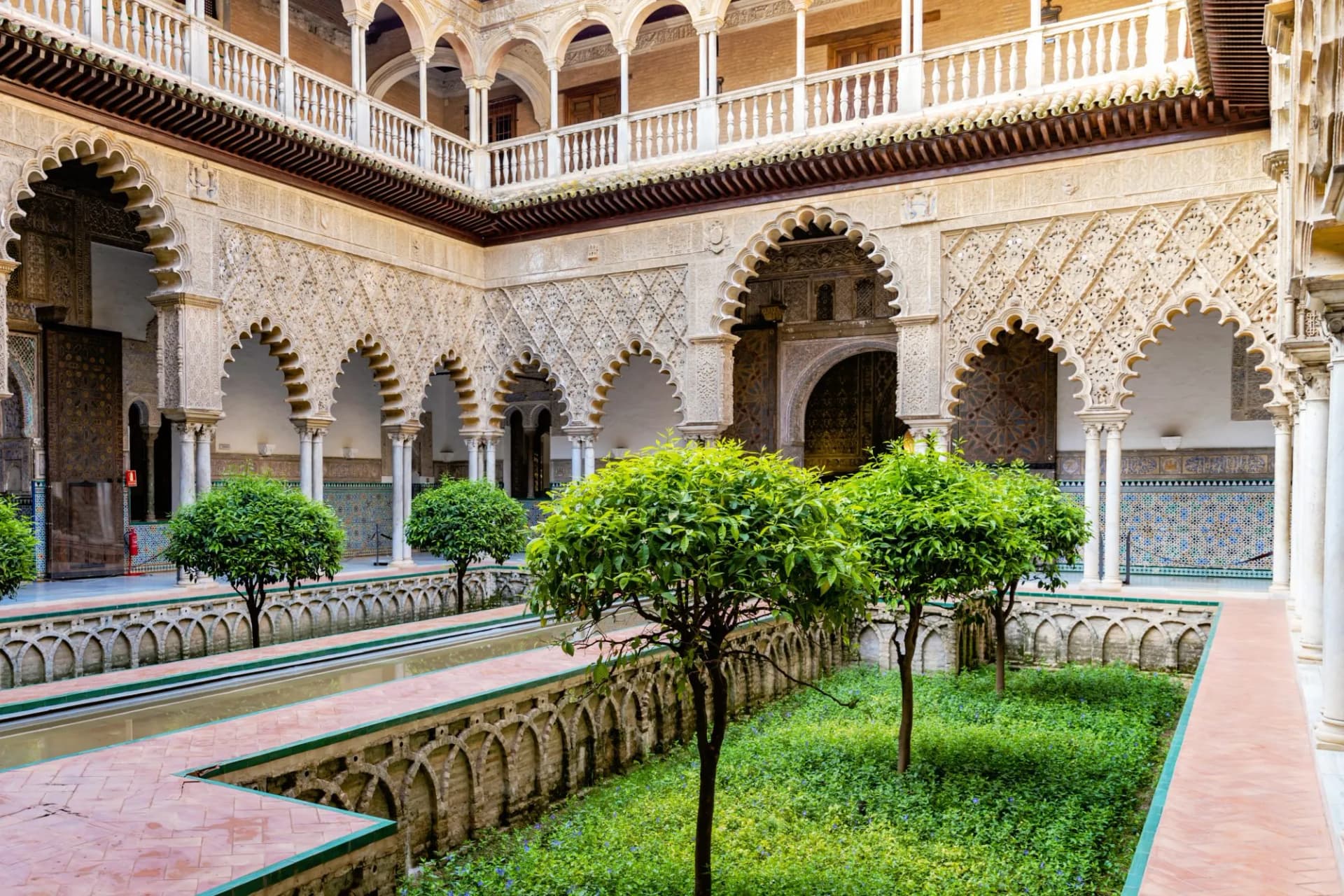 Courtyard garden with orange trees inside Alcazar of Seville Palace in Andalusia during summertime.