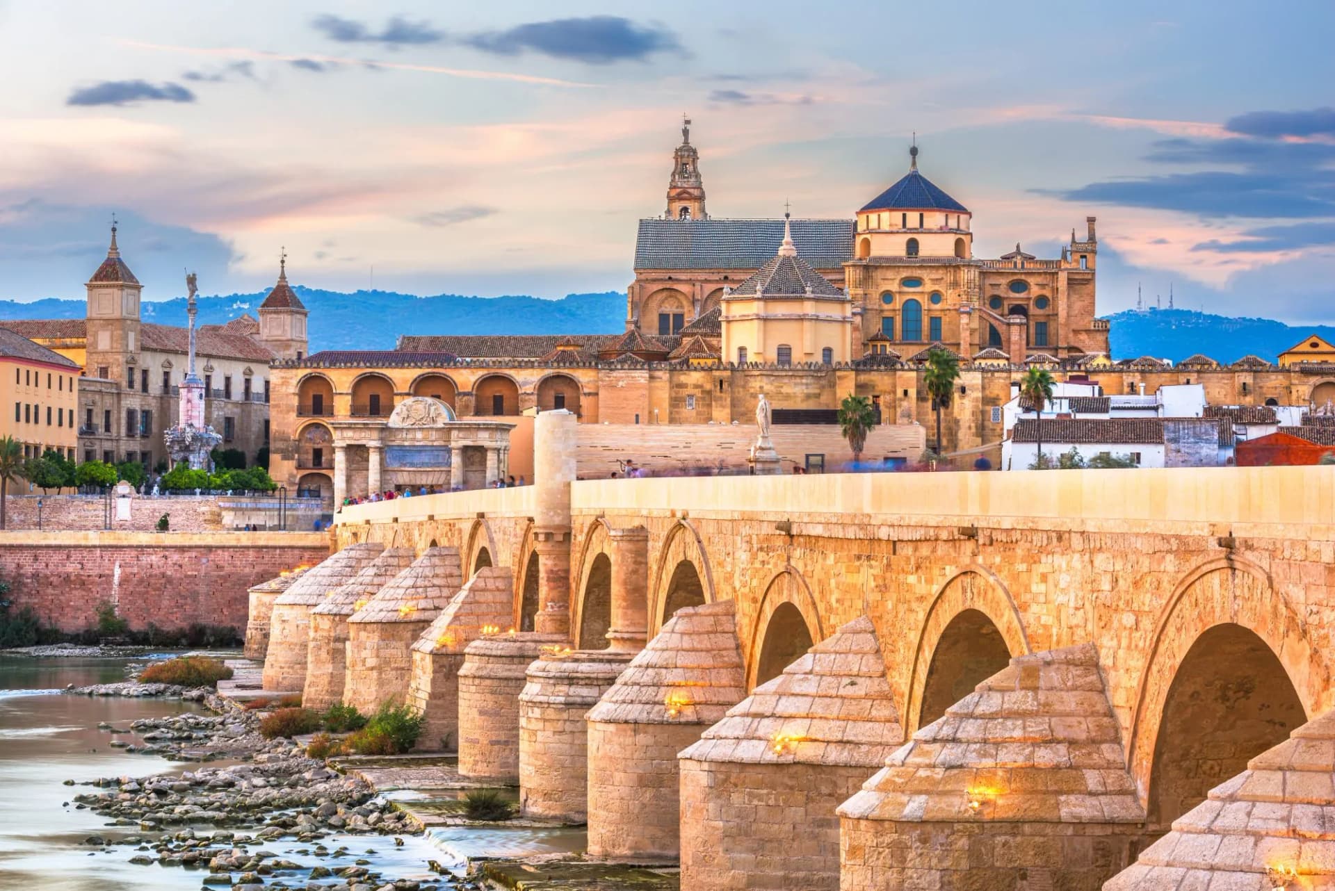 Roman Bridge and Mezquita-Cathedral in Cordoba, Spain at sunset with mountains in background.