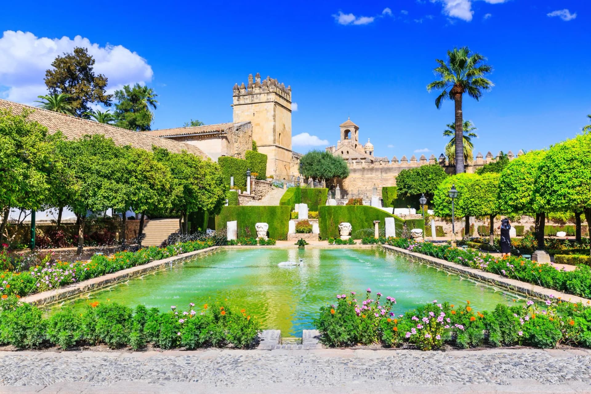 Gardens with rectangular pool and Alcázar de los Reyes Cristianos castle tower, Cordoba, Spain.