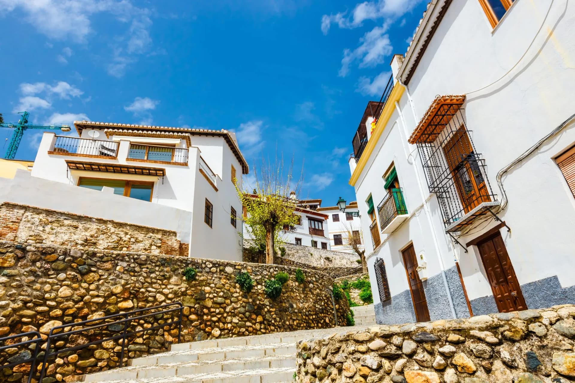 Street view of white buildings, stone retaining walls, and steps in the historic Albaicín district of Granada, Spain.