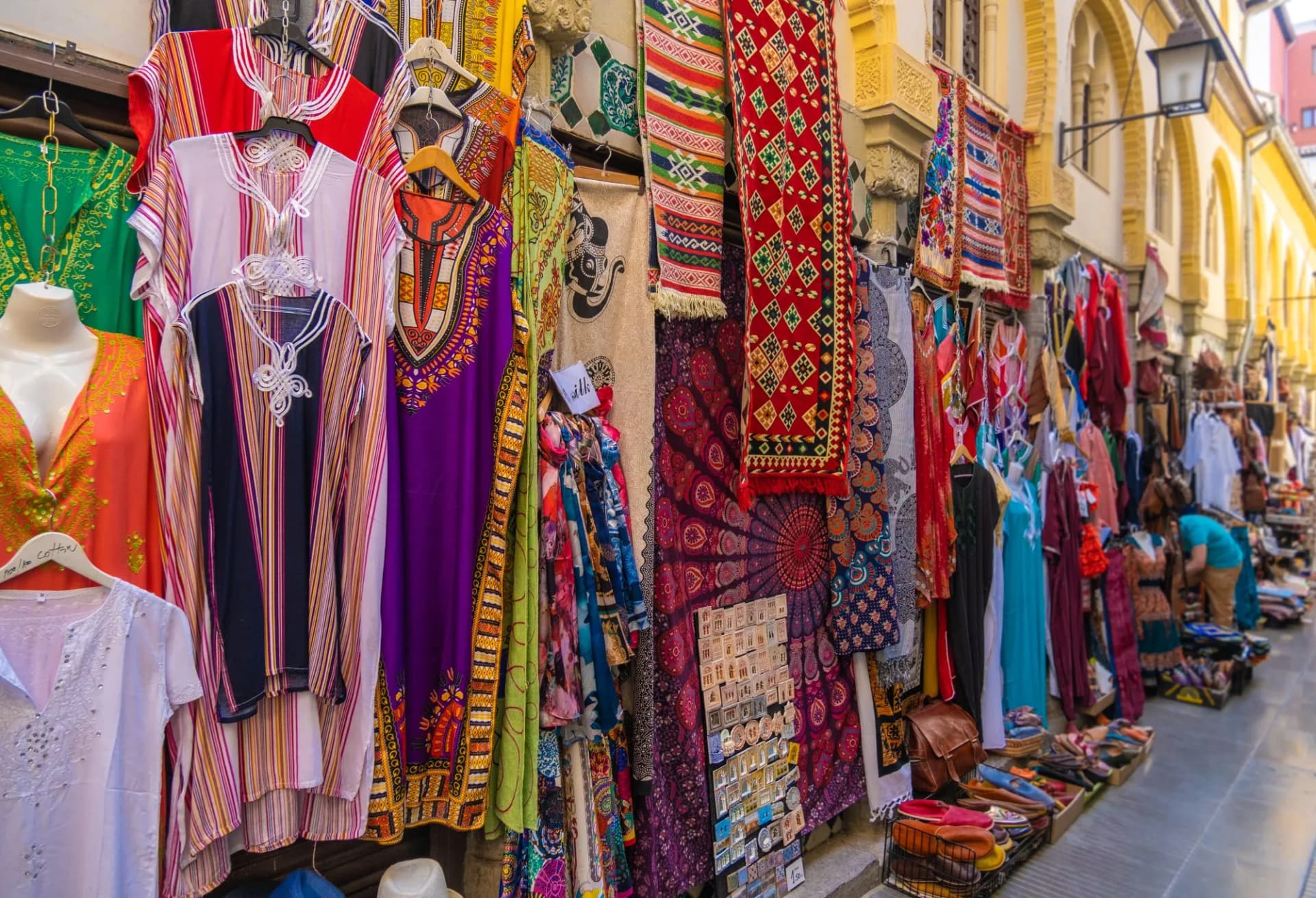 Colorful textiles and clothing displayed outside shops at the old Alcaicería Arab Market in Granada, Spain.