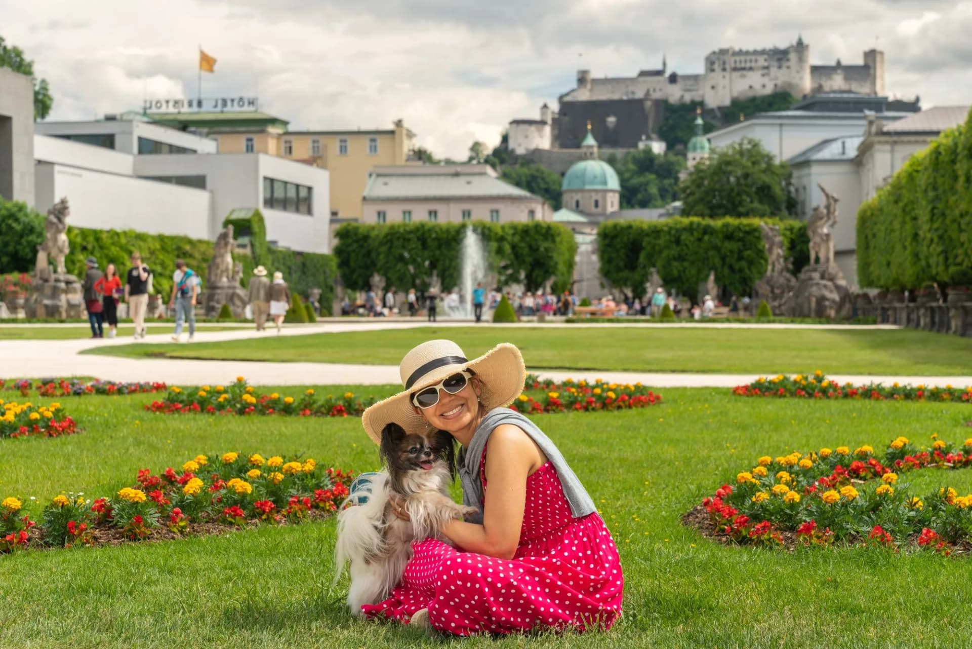 Woman with dog sitting in grass with Hohensalzburg Fortress in background, Salzburg