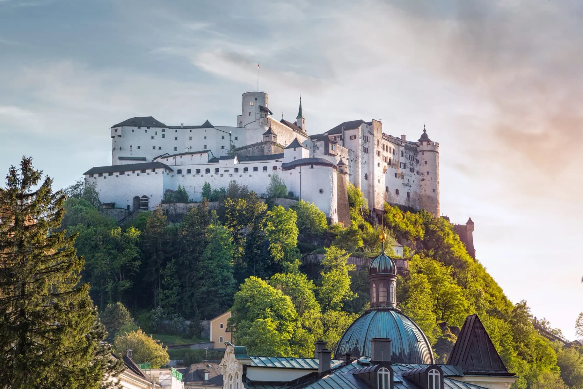 Hohensalzburg Castle above green trees and city rooftops in Salzburg, Austria.