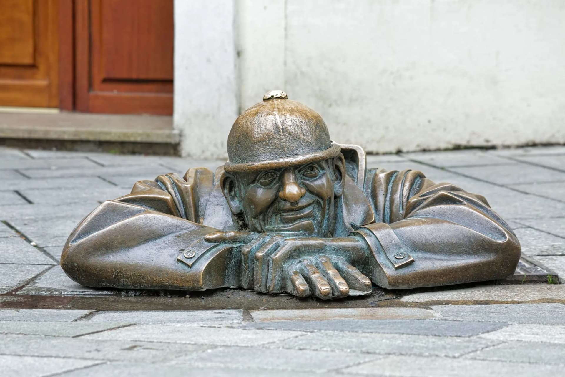 Bronze sculpture of Cumil the Peeper emerging from the pavement in Bratislava, Slovakia.