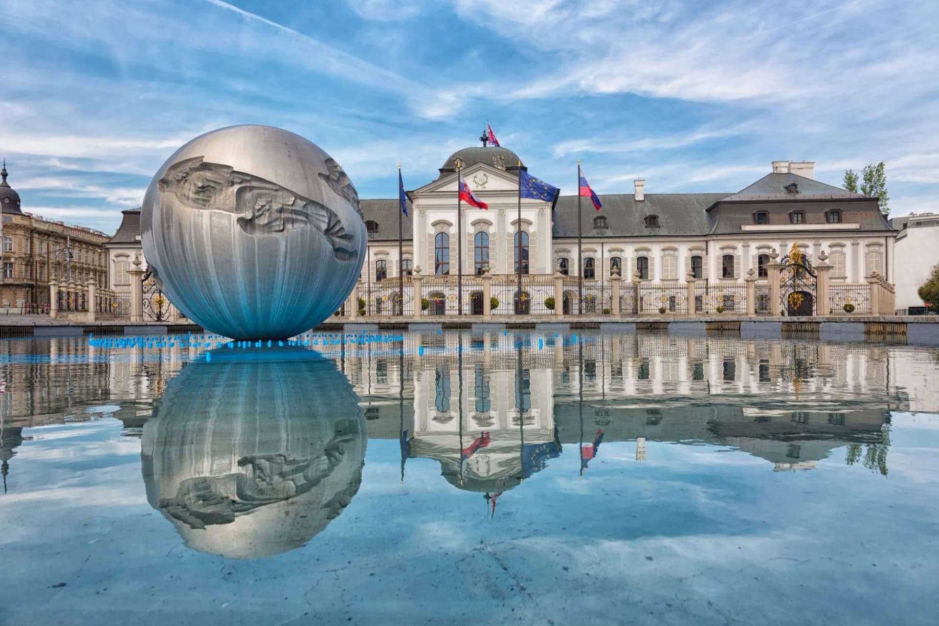 Presidential Palace in Bratislava, Slovakia, with large metal sphere sculpture reflected in water.