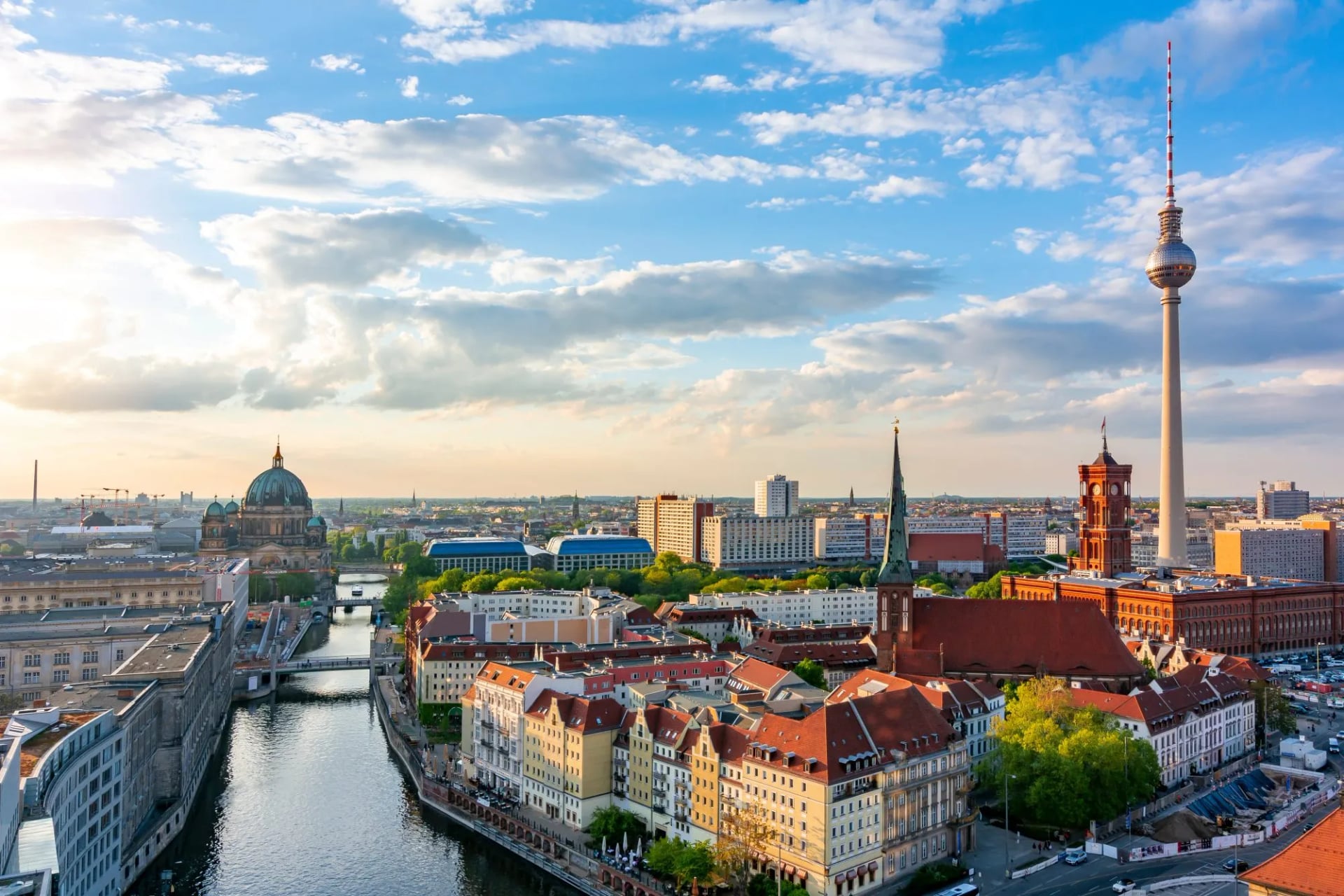 Berlin cityscape with Berlin Cathedral, Television Tower, and river under a cloudy blue sky.