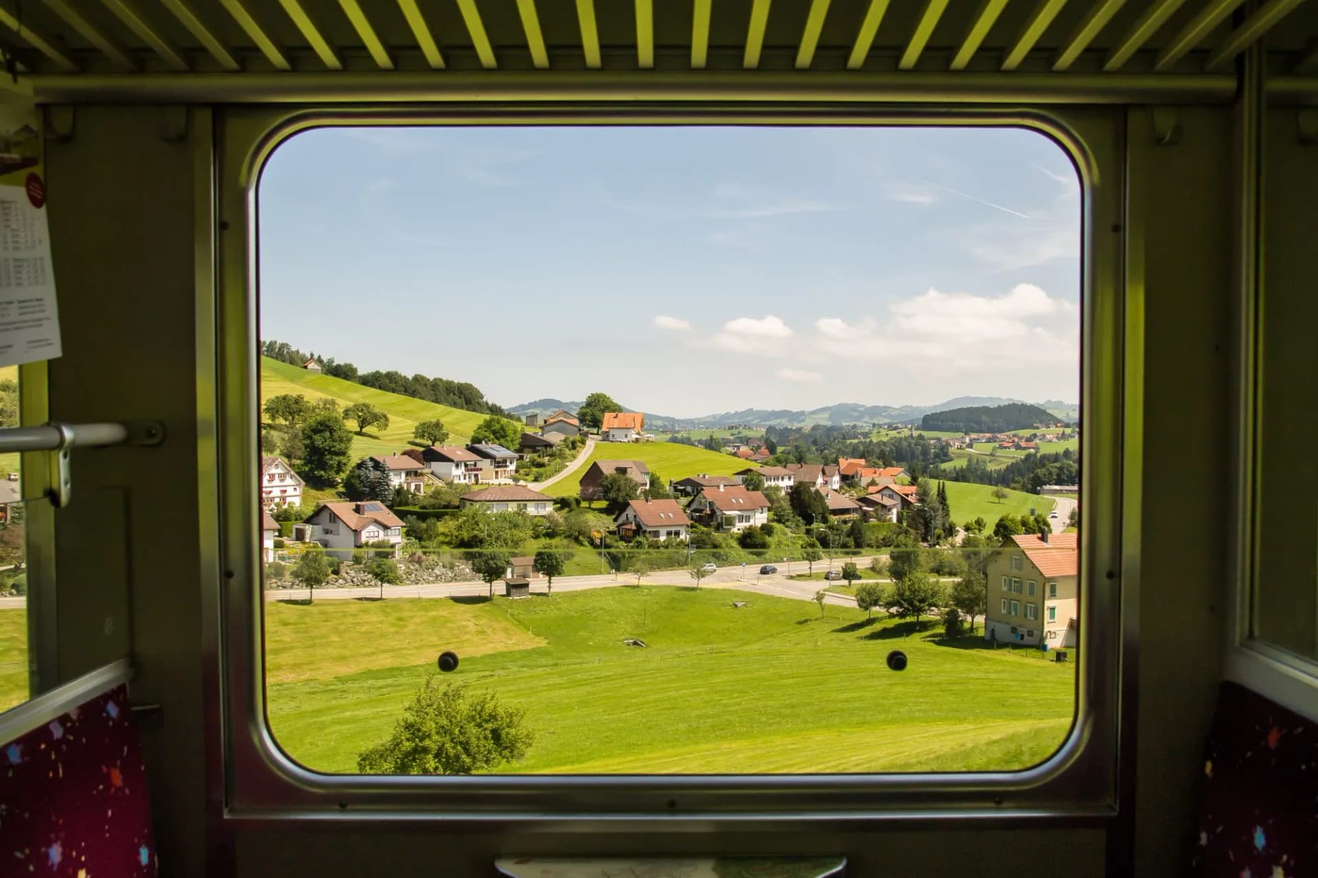 View through a train window of rolling green hills and houses near Appenzell, Switzerland.