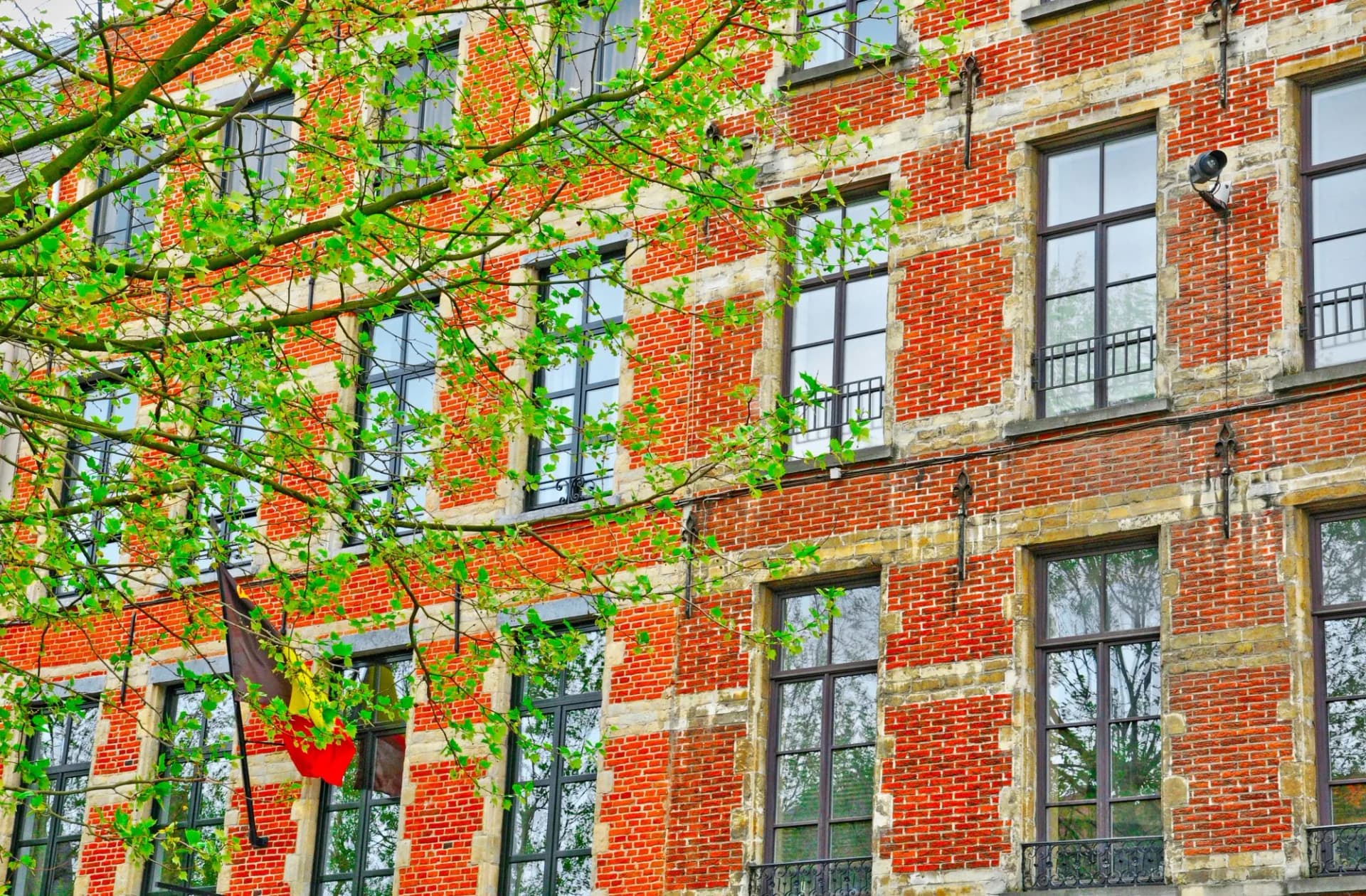 Red brick building facade with green leaves and a Belgian flag in the Sablon district, Brussels.