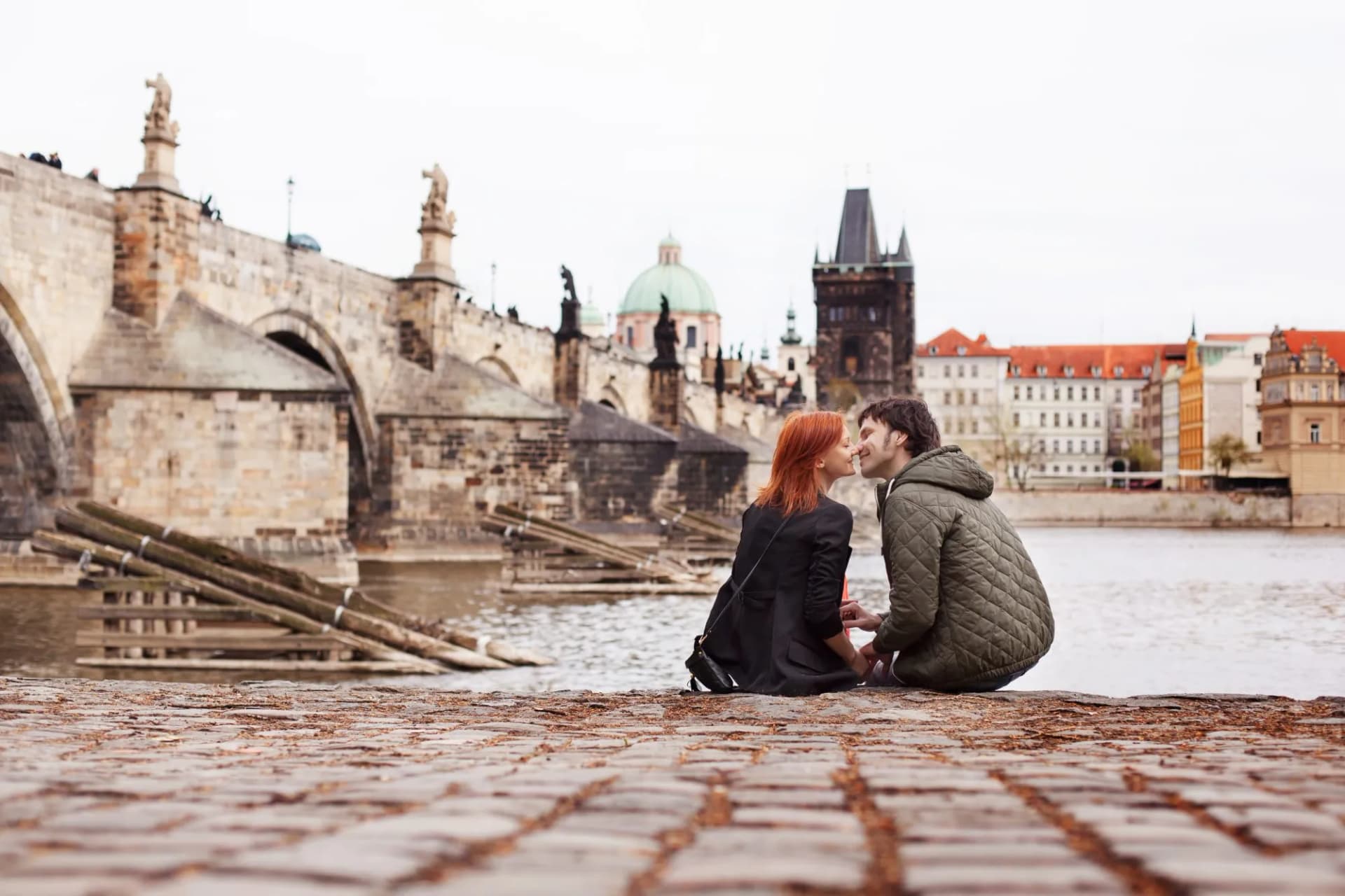Couple kissing by the river with Charles Bridge in Prague, Czech Republic