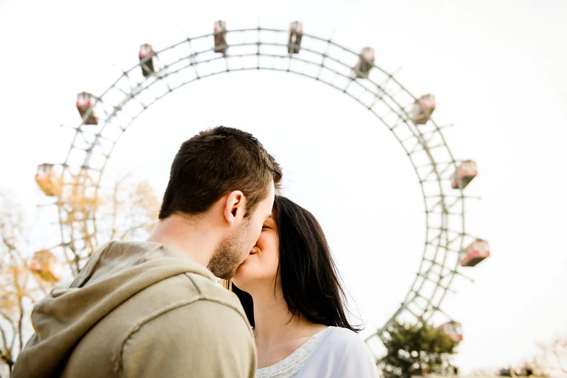 Couple kissing in front of large Ferris wheel at amusement park