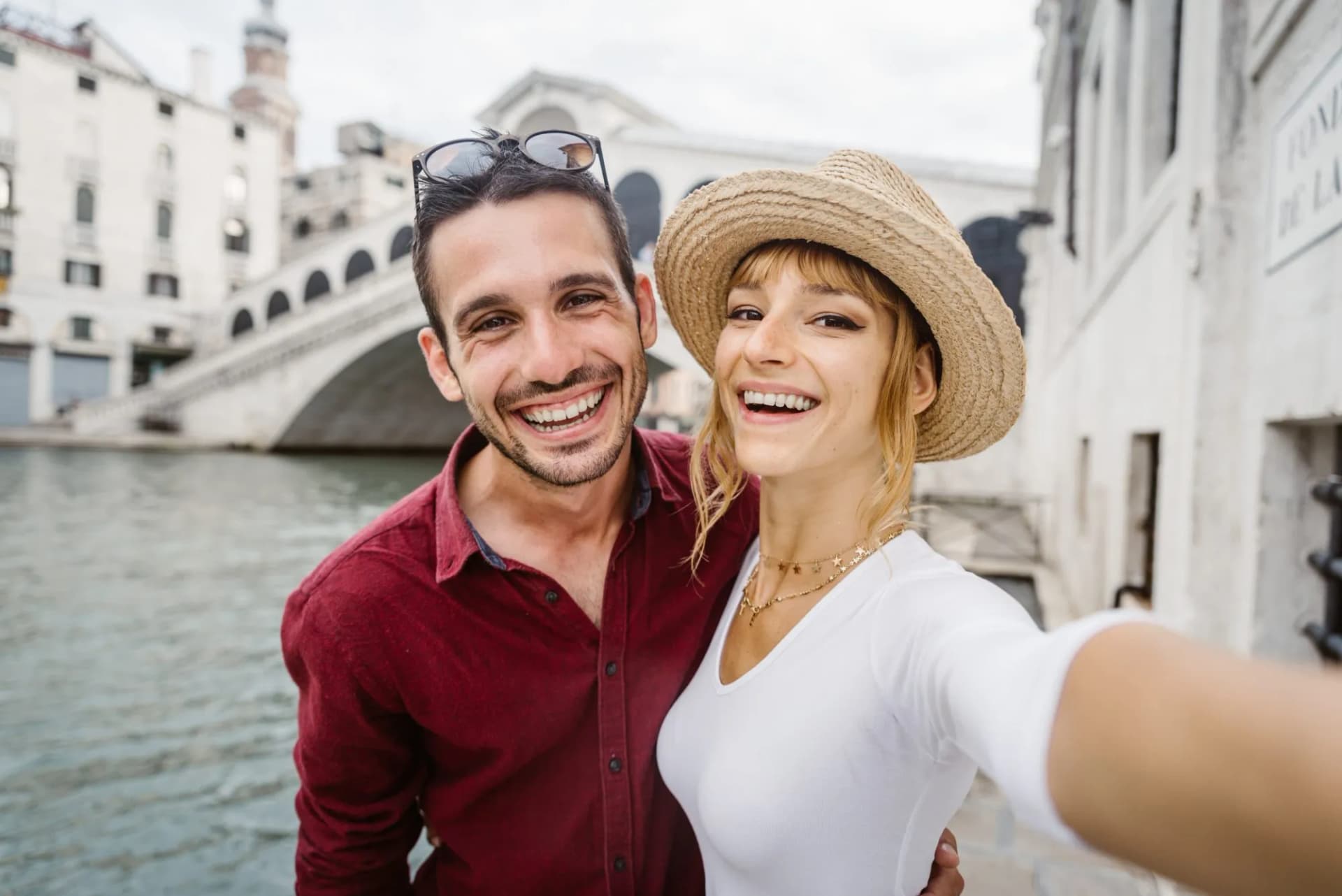 Young couple taking a selfie with Rialto Bridge in Venice, Italy in the background.
