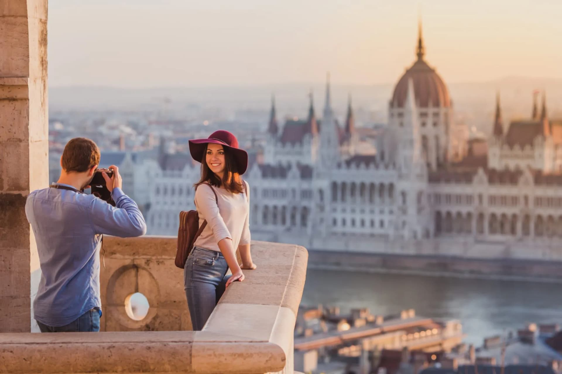 Couple taking sunrise photos on Fisherman's Bastion overlooking Hungarian Parliament Building, Budapest.