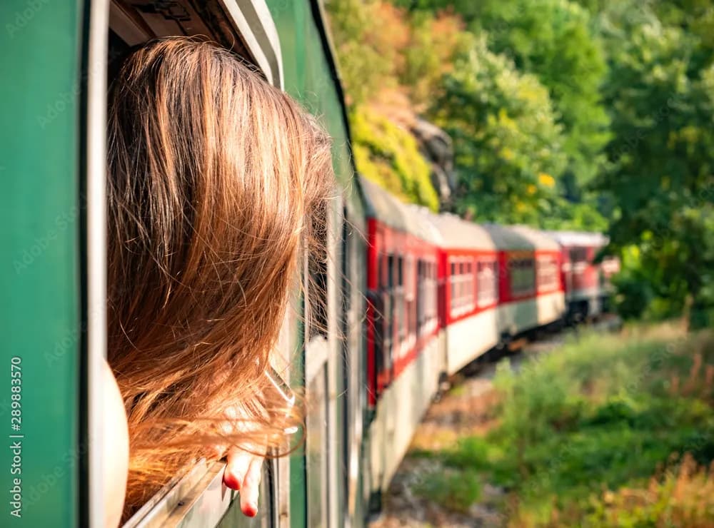 Woman leaning out of green train window traveling through Bulgarian Mountains on alpine railway.