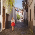 Una giovane turista bionda che esplora le strette stradine acciottolate del centro storico (Albaicin o quartiere arabo) di Granada, in Andalusia, Spagna.