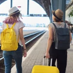 Due donne in viaggio con zaini valigia che camminano lungo la piattaforma